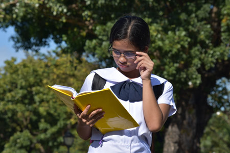 Beautiful Filipina Female Student Reading Wearing Glasses With Textbooksの写真素材