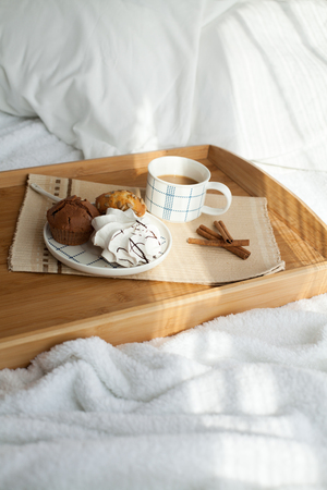 Sweet breakfast in bed with coffee and cupcakes near the window with sunlightの写真素材