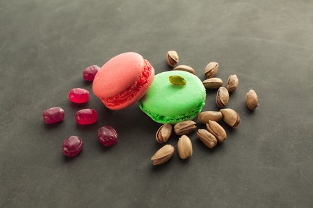 Colorful macaroons strawberry and pistachio taste, served with pistachio and candies on the dark background. Famous delicious french dessert.の写真素材