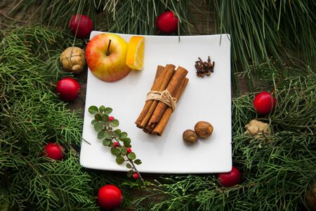 Ingredients for cooking mulled wine at home for christmas. White plate with cinnamon and fruits with branches of fir as winter decorations.の写真素材