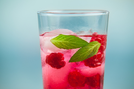 Raspberry lemonade with mint and ice on a wooden table with sea on background. Healthy fresh summer...