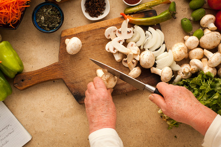 Woman slicing mushrooms with kitchen knife for cooking healthy vegetarian meal.の写真素材