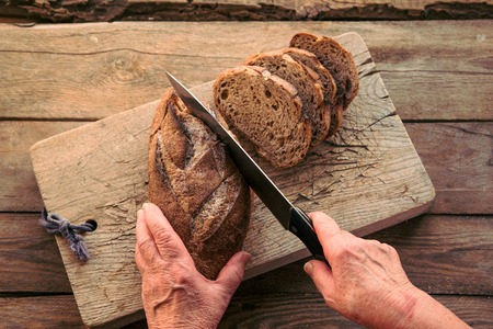 Sliced rye bread on a board. Woman cutting bread with knife for breakfast.の写真素材