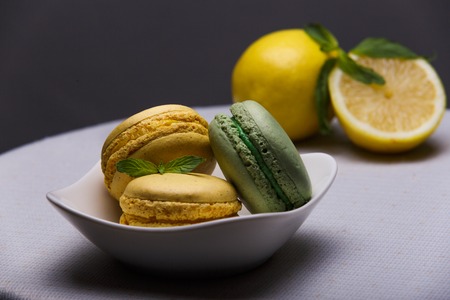Lime and lemon macaroons on white table with lemon on background and mint as a decoration. French dessert.の写真素材