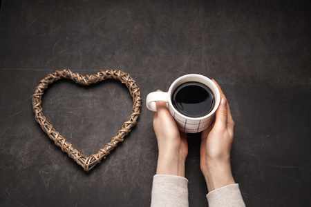 Concept of addiction to coffee in the morning. Americano into the mug on a dark background with a wooden heart shape, good for health.の写真素材