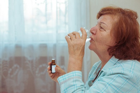 Lonely senior women drinking medicine at home. Sick old lady taking liquid medicine.の写真素材