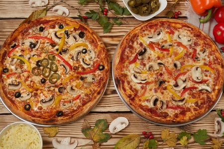 Vegetables and jalapeno pizza on wooden background with ingredients. Two homemade pizza with tasty hot pepper against other without pepper.の写真素材