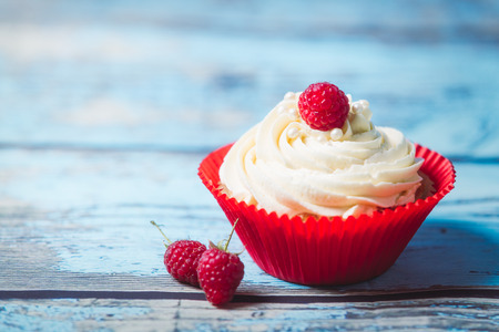 Vanilla cupcakes with cream and raspberries on a blue wooden background. Birthday muffins for a...