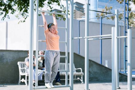 Aged woman doing sport exercises on sport ground.