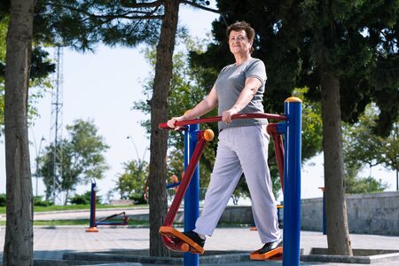 Aged woman doing sport exercises on sport ground.