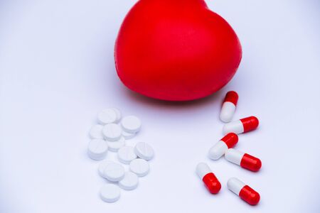 Capsule pills and round white pills with heart shape figure on white background. Symbol of cardiac treatment for sick heart. Painkiller addiction.の写真素材