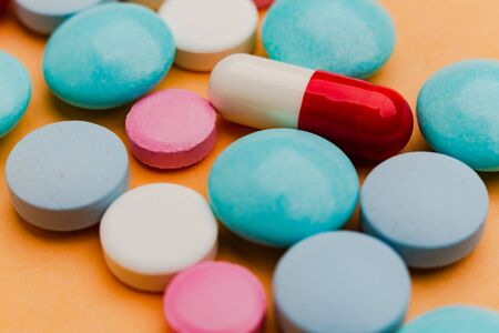 Close up of pills on orange background, concept of painkillers addiction. Lot of tablets, overdose.