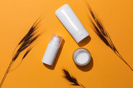 White blank cosmetic products bottles on orange background with free space for text, as advertisement. Concept of sun protection products with spf.の写真素材