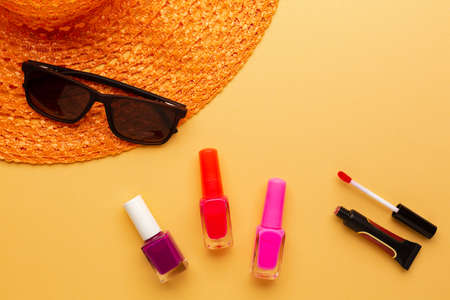 Cosmetic for making make up on summer vacation, popular colors blogger advice. Sunglasses and summer hat on orange background with decorative cosmetic products. High quality photoの写真素材