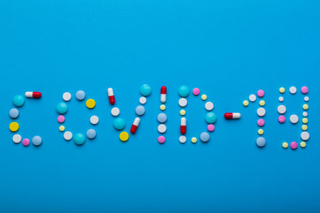 Word Covid 19 wrote with multicolored pills on blue background with free space for text. Concept of prevention from virus agitation to make a vaccine.の写真素材