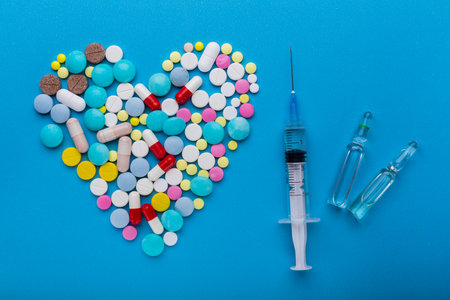 A lot of pills in heart shape and syringe with injection on blueの写真素材