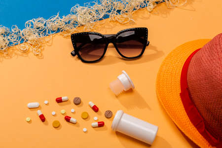 Colorful pills on orange background with sunglasses and hat. Concept of protection from allergy to the sun and sickness in the summertime on the pandemic situation.の写真素材