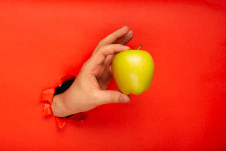 Ripe yellow apple into man's hand ripped from red color paper, concept of healthy eating and dieting. Eat an apple a day keep the doctor away.の写真素材
