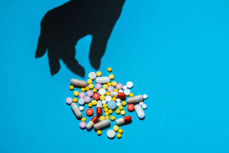 Shadow from hand taking a pill from the heap of pills on blue background. Concept of taking pills by prescription.の写真素材