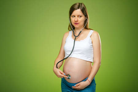 Pregnant woman with stethoscope trying to hear her baby heartbeat by herself. Worrying in pregnancy.
