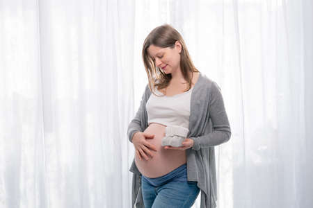 Pregnant Woman Belly. Pregnancy concept. Pregnant Woman holding Baby Shoes in her Hands. Mom Expecting Baby. Baby Shower.の写真素材