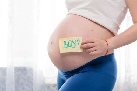 Pregnant woman with a big belly, gender party, holding boy signed paper in hand. It is a boy.の写真素材