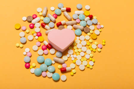 Different pills with heart figure on an orange background, the concept of medical prevention heart attacks. Cardiologists advise how to treat your heart to be healthy.の写真素材