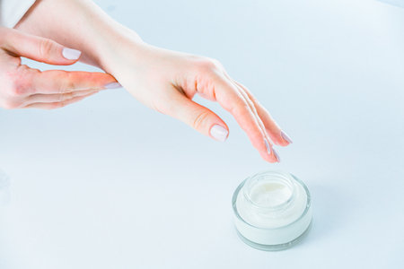 Close-up of female hands applying moisturizing cream on white backgroundの写真素材