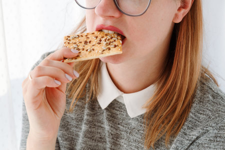 Close-up of womans mouth eating no sugar cookie with sesame seeds, pastry for dietary mealの写真素材