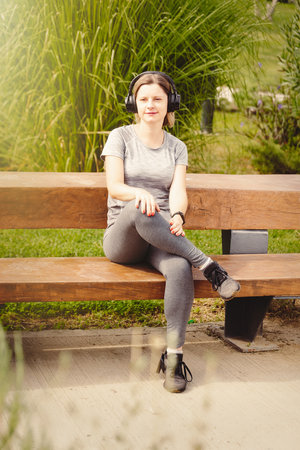 A woman in a headset listening to music and singing, in a good mood after training, in a city park.の写真素材
