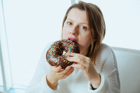 Woman eating chocolate glazed donut, dieting theme.