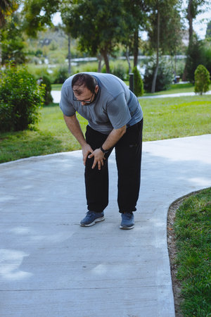 Man with extra weight jogging in park in the morning and feels pain in his knee.
