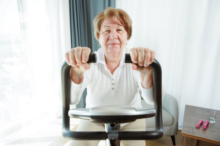 Senior woman training at home on a bicycle trainer, healthy lifestyle after retirementの写真素材