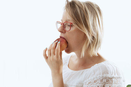 Young woman biting peach, healthy snack on a lunchtime, sweet and organicの写真素材