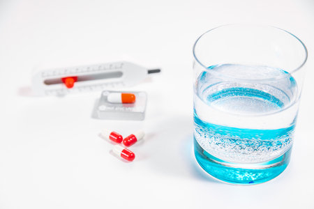 A glass of water with pills, a thermometer, and antibiotics for recovery from a virus.の写真素材