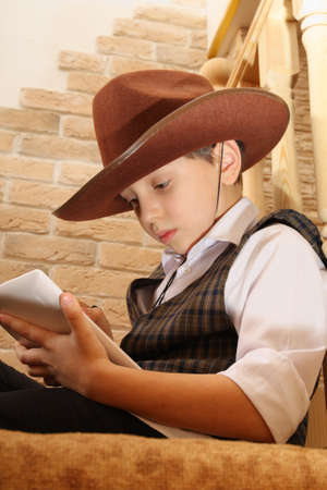 Boy as a cowboy reading on a tablet, sitting somewhere in a secluded placeの写真素材
