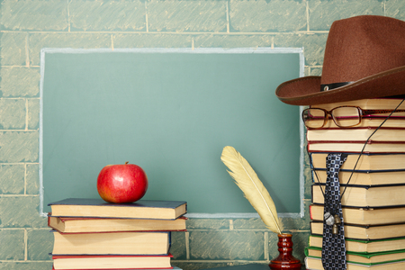Funny education idea: the teacher, books, quill pen, apple before blackboard with copy spaceの写真素材