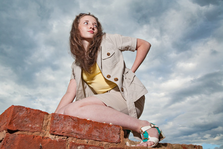 Fashionable girl posing on old brick wall on sky backgroundの写真素材