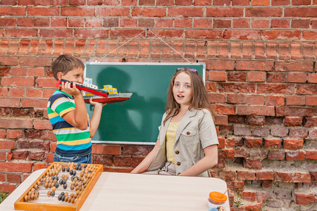 The boy shows to the young teacher the ships made by him in the improvised class