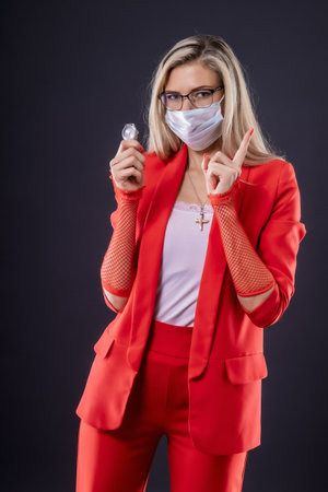 A young woman with a watch in her hand and a mask on her face warns of danger by gesturing with her index fingerの写真素材