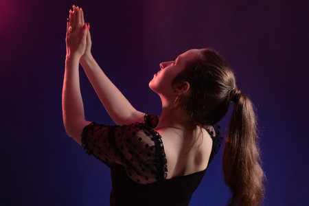Portrait of a beautiful young girl with hands raised to the sky in color backlight