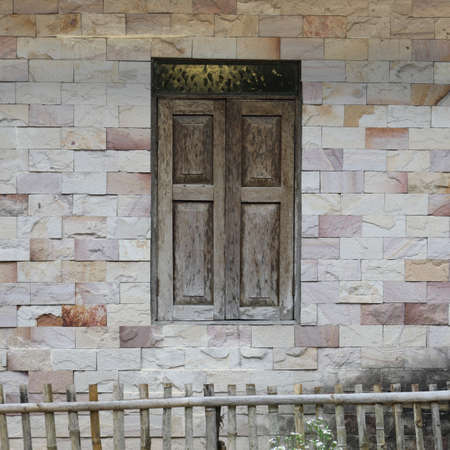Wall of house made from mortar with tile is rectangular and it is window with bamboo fence.