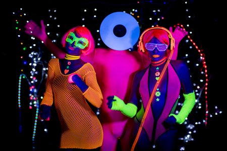3 cyber glow raver friends filmed in fluorescent clothing under UV black lightの写真素材