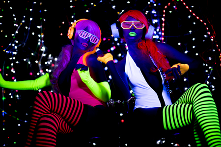 2 sexy cyber glow raver women filmed in fluorescent clothing under UV black lightの写真素材