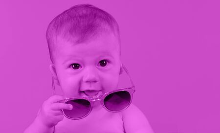adorable small baby girl holding sunglasses, against plain colour backgroundの写真素材