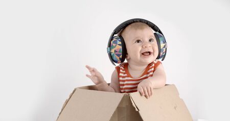 adorable small baby girl in a box with headphones  against whiteの写真素材