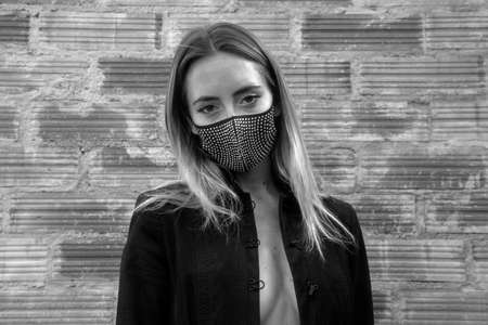 Young woman wearing sparkly black face mask against brick wallの写真素材