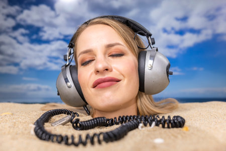 Woman buried in sand on beach with headphonesの写真素材