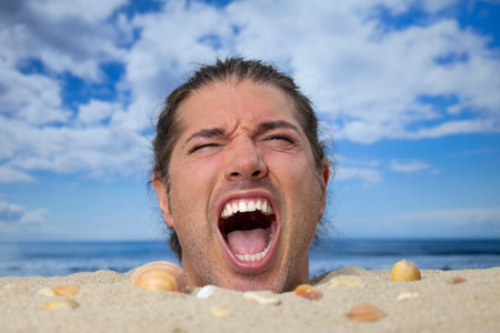 A man buried in sand on beach screamingの写真素材