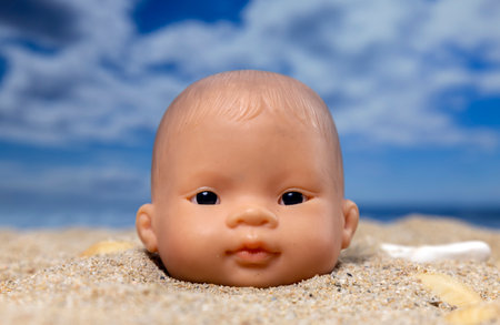 A baby doll head buried in sand on beach